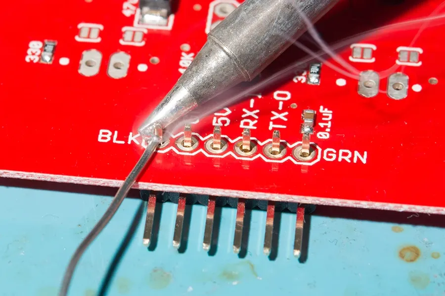 A PCB with through-hole components being soldered by hand.