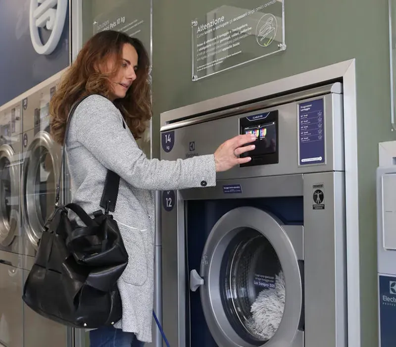 A person using a self-service laundry machine with a detergent vending machine nearby